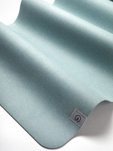 High-quality teal yoga mat with textured surface and branded label visible, angled side view shot highlighting durability and grip design.