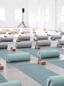 Blue yoga mats neatly arranged in a bright studio with rolled towels and blocks, serene calm atmosphere for meditation and exercise, no visible brand, side view.