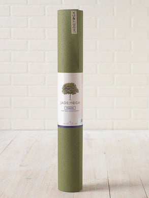 JadeYoga Travel yoga mat rolled up in olive green color with brand label against white brick wall background, eco-friendly high-grip yoga mat, side view
