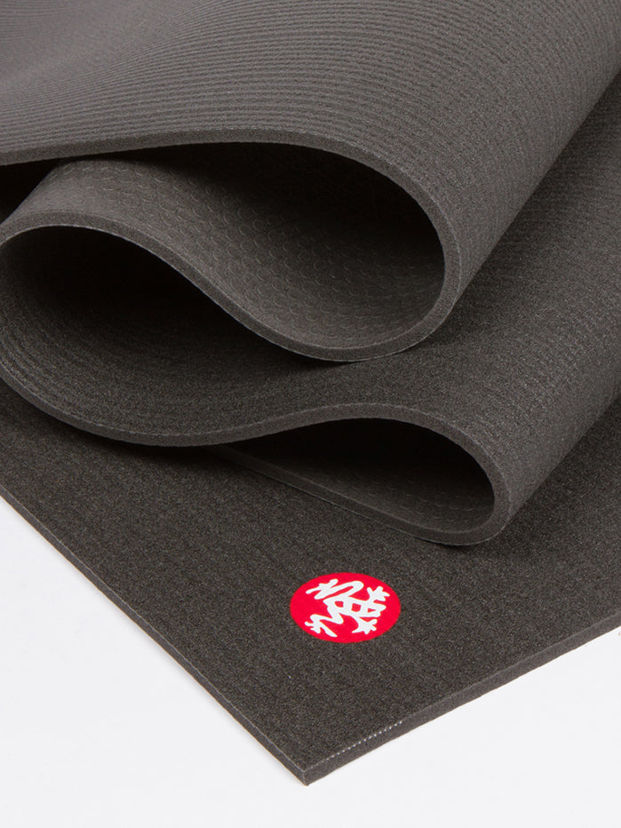 Black textured non-slip yoga mat partially unrolled showing the side and thickness with a visible red brand logo on the front, fitness and exercise equipment.