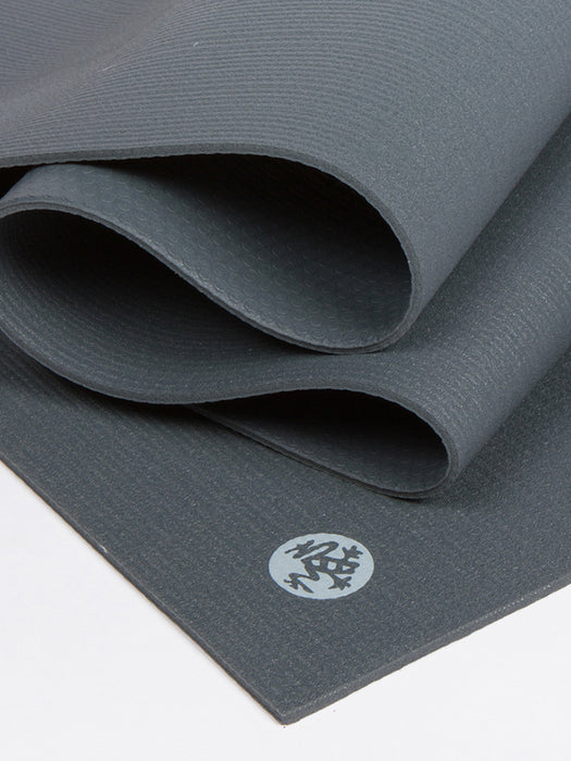 Dark gray textured yoga mat partially unrolled with visible logo, non-slip surface, close-up side shot.