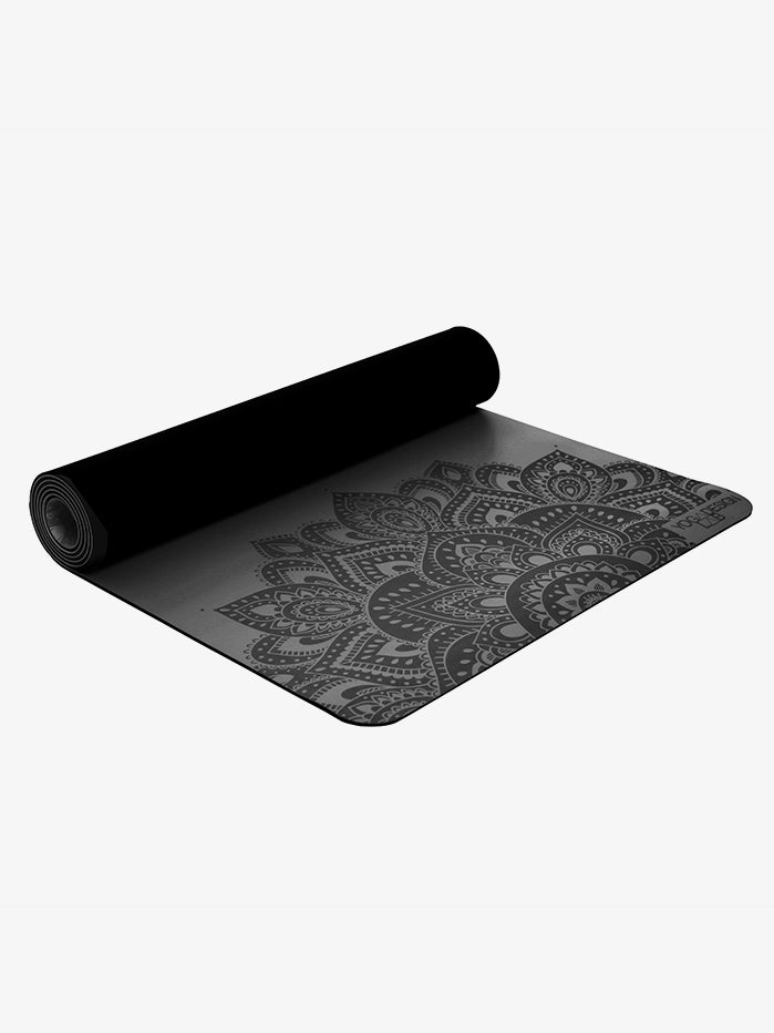 Black yoga mat with intricate mandala pattern, non-slip texture, side angle view, rolled halfway for product detail display