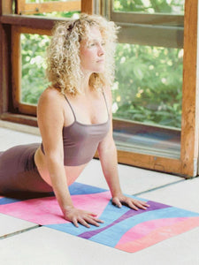 Woman practicing yoga on a colorful geometric pattern yoga mat inside a room with natural light, side view.