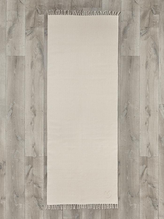 Beige yoga mat with fringed edges on wooden floor, top view, no visible branding