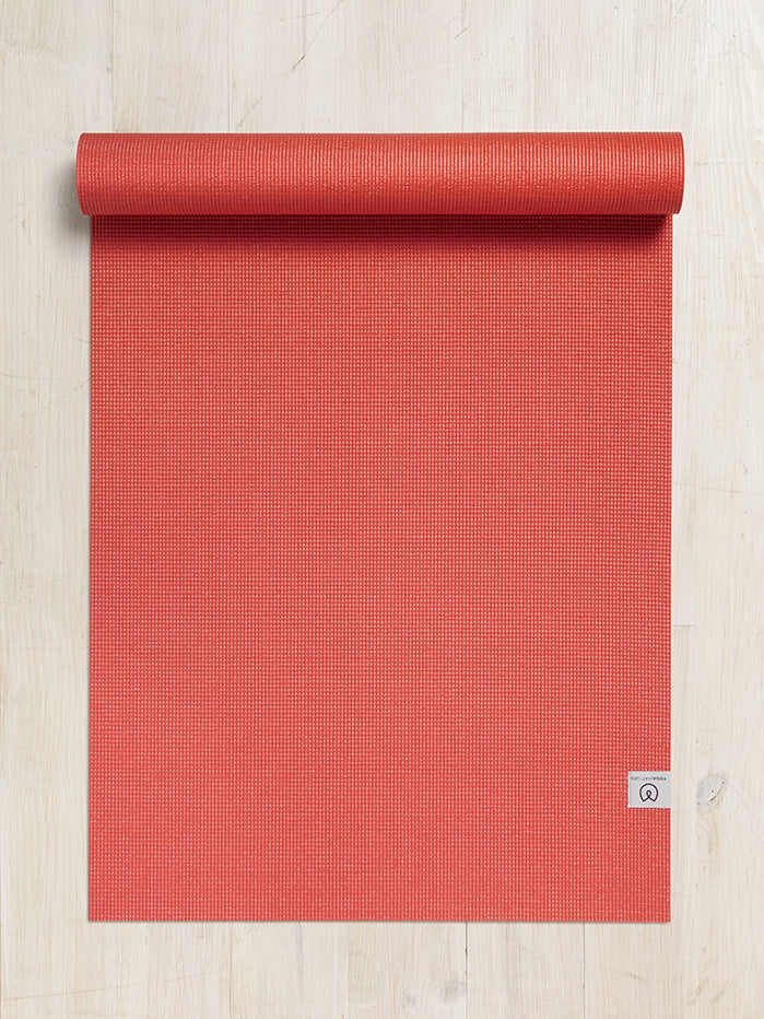 Red textured yoga mat partially rolled up on a hardwood floor, top view with visible logo.