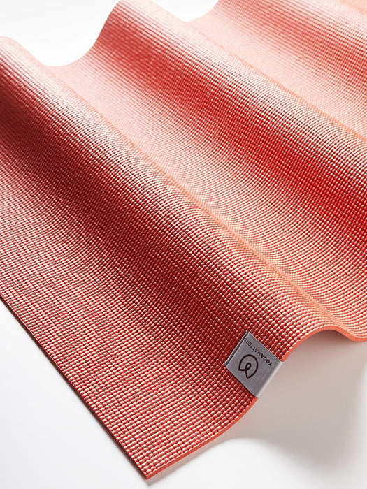 Coral red high-grip textured yoga mat from side angle showing brand logo, ideal for Pilates and yoga practice
